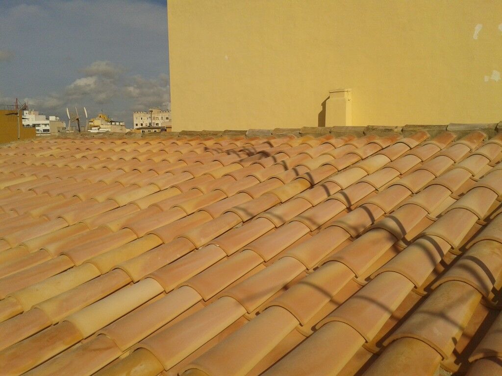 Faldón de teja nueva junto a una pared enfoscada en amarillo